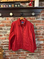 Front view of red Karen Scott sport jacket hanging on a hanger against a brick wall background.
