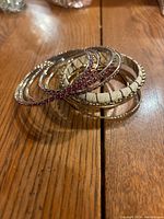 Several bangle bracelets stacked on a wooden surface, showing jeweled and textured designs.