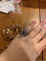 Photo showing four rose gold colored bangle bracelets and four assorted rings on hand, including butterfly and fleur-de-lis designs.