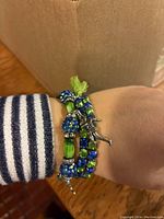 Close up of wrist wearing two stretchy rhinestone bracelets in blue and green with a silver toned Seahawk player charm and decorative beads