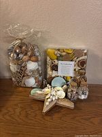 Overview photo showing bag of potpourri with seashells, boxed seashell potpourri, and wooden star ornament with seashells on a wooden surface