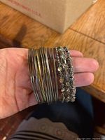 Hand holding multiple silver-tone bangle bracelets, showing plain and jewel-embellished bangles stacked together.
