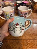 Photo showing a blue snowman mug with three snowmen in a snowy forest scene
