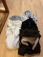 Six folded sweatshirts arranged on a wooden floor, showing mix of colors and styles.