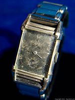 Photo of front of vintage Bulova tank style wristwatch showing rectangular gold-filled case, worn and aged dial with sub-second dial, metal band.