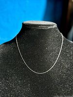 Thin 10KT white gold necklace displayed on black textured mannequin stand, showing the length and delicate design.