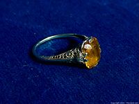 Side-angle view on blue background showing filigree shoulders and prong-set yellow topaz