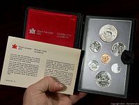 Photo showing set of seven Canadian coins in black case with red lining and certificate card from Royal Canadian Mint in hand.