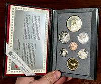 Front view of the coin set in original black and red packaging showing all seven coins in foam insert.