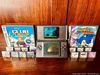 Overview of open DS Lite console with game cases and loose cartridges arranged on wood surface