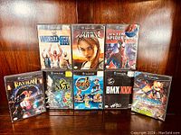 Overall view of all eight Nintendo GameCube games in their cases, standing upright against a wood background. Games shown include Wrestlemania XIX, Tomb Raider: Legend, Ultimate Spider-Man, Rayman Arena, Dr. Muto, Disney's Extreme Skate Adventure, BMX XXX, and Starfox Assault. All cases closed and appear complete except Starfox missing manual noted