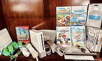 Overall view of white Wii console, vertical stand, power adapter, AV cable, controllers, manual, and game cases
