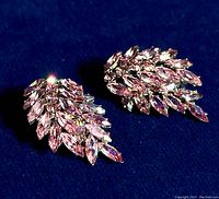 Pair of Sherman vintage pink rhinestone leaf earrings under direct light on dark fabric background showing top view and sparkle.