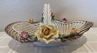 Side view of vintage porcelain Capodimonte basket featuring woven texture, large yellow rose with smaller pink roses and green leaves on the rim, and twisted handle.