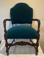 Front view of the green velvet armchair showing fabric upholstery and wooden arms and legs.