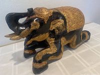 Angled front view of a black and gold gilt mahogany elephant figurine embellished with small jewels and lacquer, showing raised trunk and ornate details.