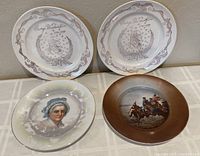 Four ceramic plates laid out on a table: two white with George Washington designs, one with portrait of Martha Washington, and one brown-bordered with historical scene