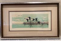 Framed lithograph of geese flying over water and marsh with natural tones and artist signature visible.