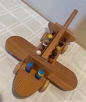 Top angled view of wooden toy airplane loaded with passengers and pilots, showing natural wood finish and rounded design.