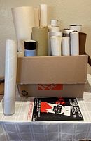 Box of rolled posters with one poster displayed on table with black background, white text, and red flame graphic