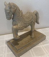 Front angle view of horse statue showing raised front leg, ornate saddle, pedestal base, and overall pose.