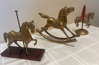 Photo showing all three brass horses together: large rocking horse, wooden base carousel horse, and round base carousel horse with ribbons.