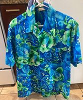 Front view of vintage Hawaiian shirt showing bright blue and green floral design with silver buttons.