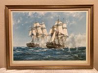 Framed color lithograph depicting a naval battle with two sailing ships firing cannons.