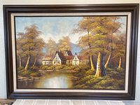 Frontal image showing the entire framed oil painting of a house by a pond surrounded by trees and distant mountains in a fall setting.