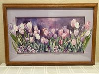 Framed watercolor painting of tulips with purple, white, pink flowers and green leaves. Double matting shows extension of tulip artwork beyond main painting. Light brown wood frame.