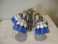 Chandelier fully assembled, showing five stained glass shades in white and blue on a bronze frame, lying on a white tablecloth.