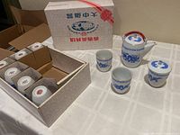 Photo showing the original box, six covered cups in box, three uncovered cups and lidded teapot on table