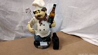 Front view of resin chef figurine holding liquor bottle, leather cradle beside