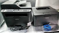Both Brother printers side by side with power cords and Ethernet cable visible