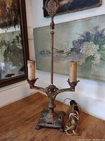 Full view of the antique bouillotte lamp showing ornate metal construction, two candle-style light arms with faux wax candle sleeves, and the central decorative finial.