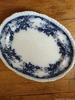 Full view of the antique Flow Blue platter showing the oval shape, floral blue patterns, and embossed scalloped edge.