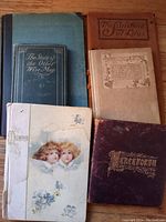 Top view of six antique small books arranged, showing various decorative covers including green, brown, beige, and purple covers, one with image of two children.