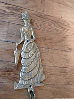 Front view of brass Southern bell figure plant hanger showing detailed dress, hat, and umbrella held by figure standing on floor.