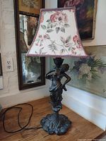 Full view of lamp showing bronze style figurine base with floral fabric shade in room setting.
