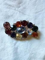 Top view of colourful rhinestone brooch showing various amber, red, green, blue, yellow and iridescent stones in gold-tone setting.