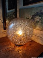 Clear glass globe lamp approximately 12 inches in diameter with intricate silver wire design inside, lit to show inner light effect.