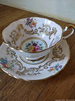 Porcelain teacup and saucer set displaying the floral and gold decorative design from above and side view