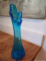 Blue swung glass vase with wavy edges, gradient blue color, standing on wooden surface