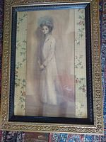 Full view of framed pastel sketch showing the young woman in a large hat with floral fabric matting and ornate gold frame.