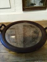 Full view of round antique tray with wooden frame, handles, and glass insert