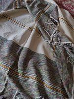 Woven cotton throw with white base and multicolored stripes with fringed edges displayed on a surface.