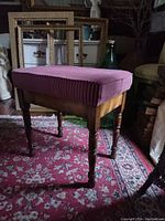 Full view of wooden stool showing striped maroon upholstery and turned legs on a patterned carpet.