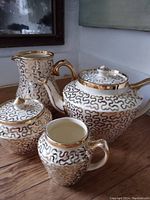 Photo of four-piece ceramic set with teapot, creamer, sugar bowl, and pitcher with gold squiggle pattern and gold rims/handles/lids.