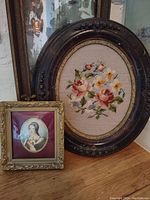 Photo showing both the needlepoint floral in oval frame and the Lady Jane Gray print in gold frame on wooden surface with mirror background
