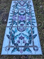 Full view of all three stained glass panels laid side by side on grass